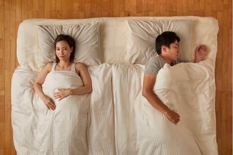 Sad wife laying next to sleeping husband