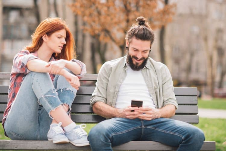 Young jealous woman looking at man text messaging