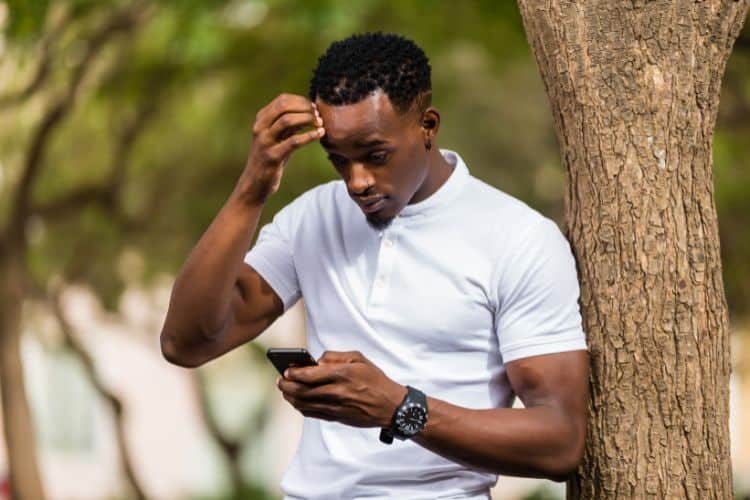 Young man at a park with his phone stressed while texting