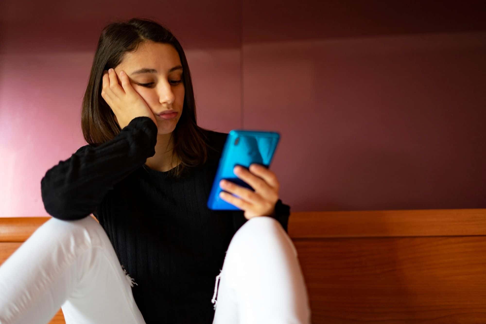A woman looking at her smartphone with a concerned or weary expression, representing the pressure of constant validation-seeking in a relationship.